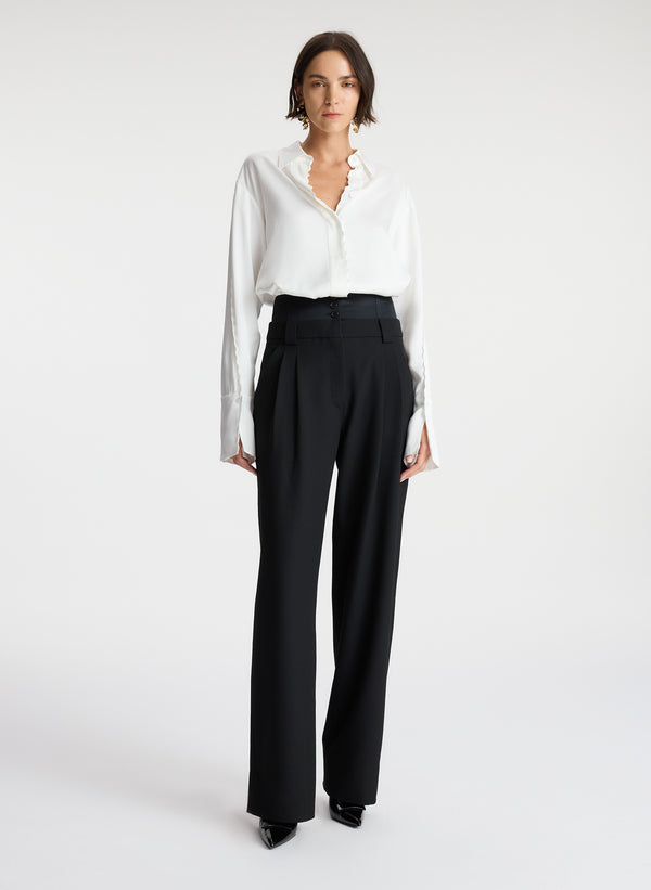 front view of woman wearing white scalloped detailed long sleeve top and black pants