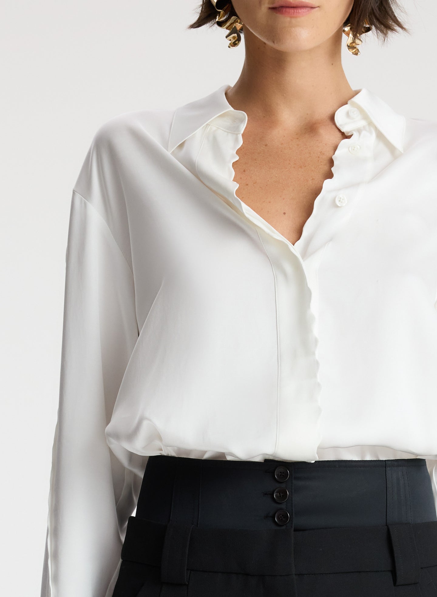 detail view of woman wearing white scalloped detailed long sleeve top and black pants