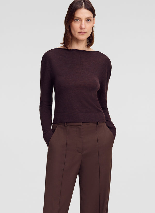 A woman modeling a dark brown long-sleeve knit top with a wide boat neckline, paired with brown trousers, against a light gray studio background.
