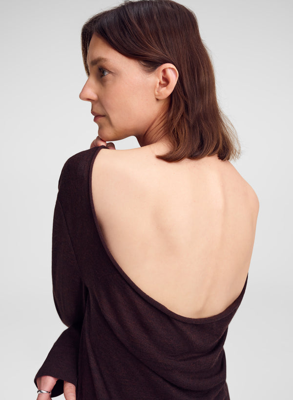 A woman shown from the back wearing a dark brown draped top with a very large open back, photographed against a light gray studio background.