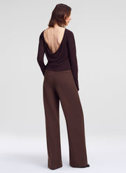 A model shown from the back wearing a dark brown long-sleeve top with a dramatic open back and matching wide-leg trousers, set against a plain light gray studio background.