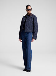 Person wearing a navy quilted jacket and sunglasses on a light gray background