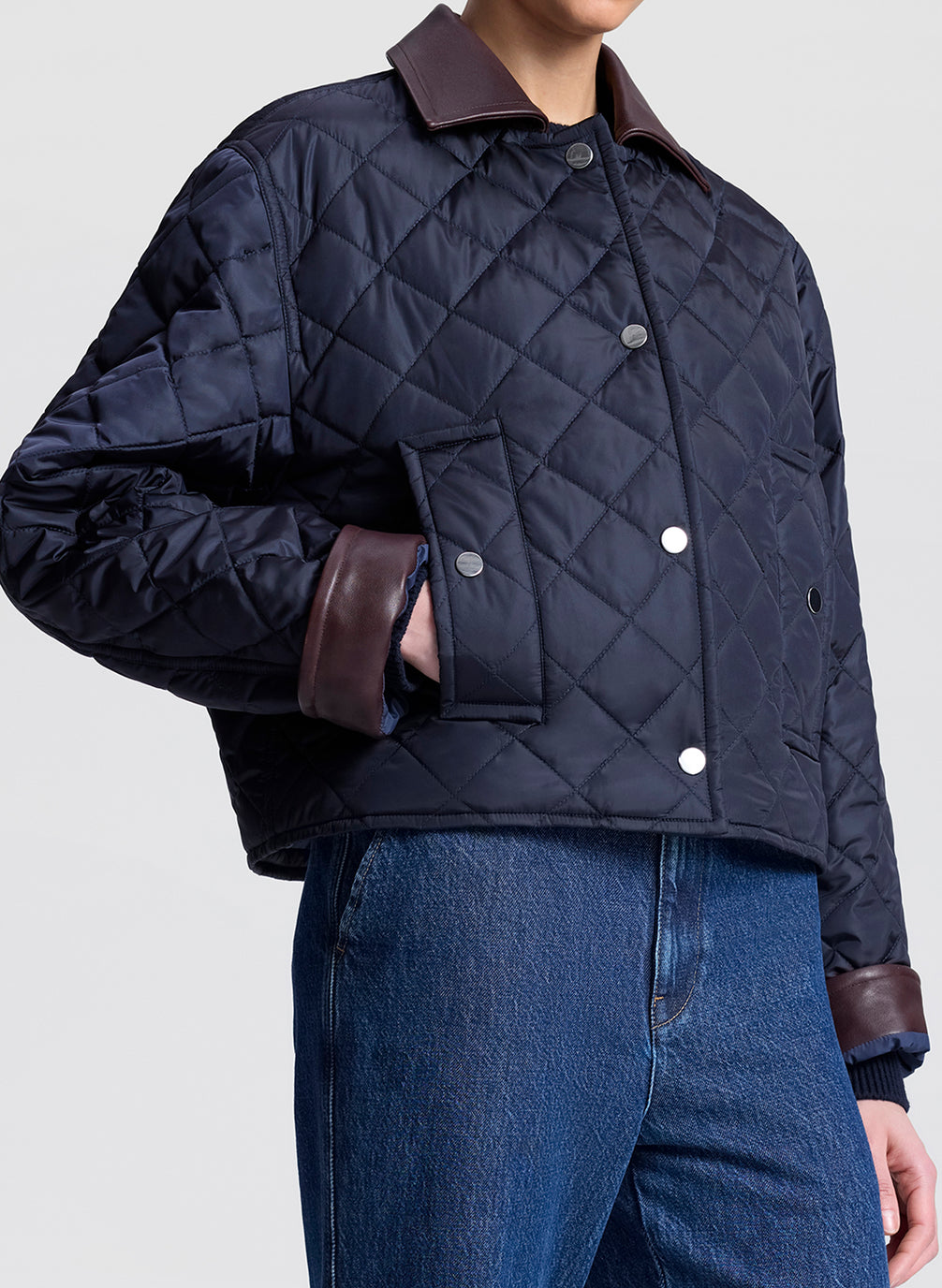 Person wearing a navy quilted jacket and sunglasses on a light gray background
