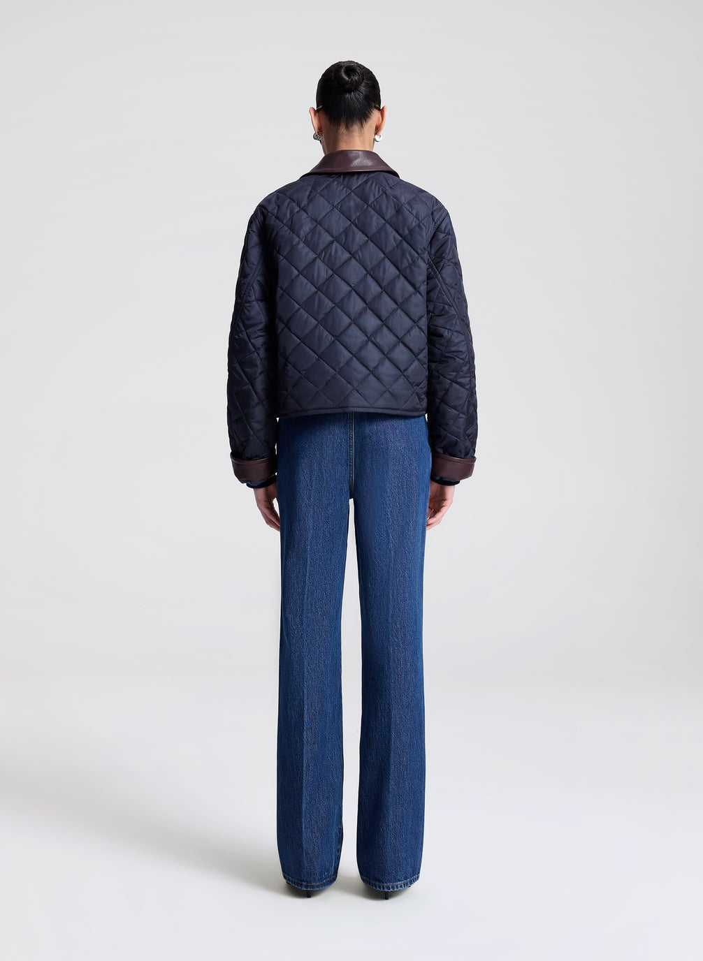 Person wearing a navy quilted jacket and sunglasses on a light gray background