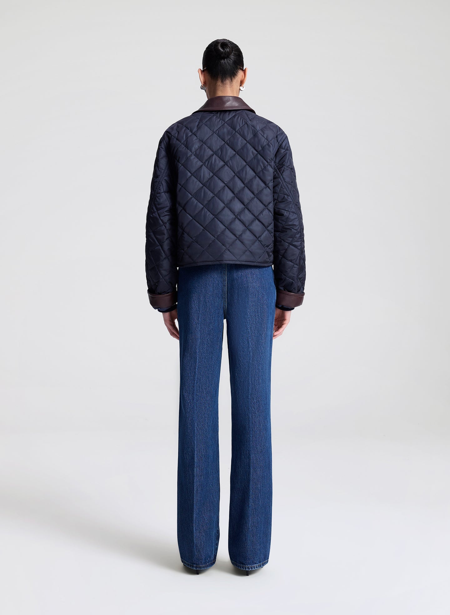 Person wearing a navy quilted jacket and sunglasses on a light gray background