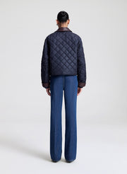 Person wearing a navy quilted jacket and sunglasses on a light gray background