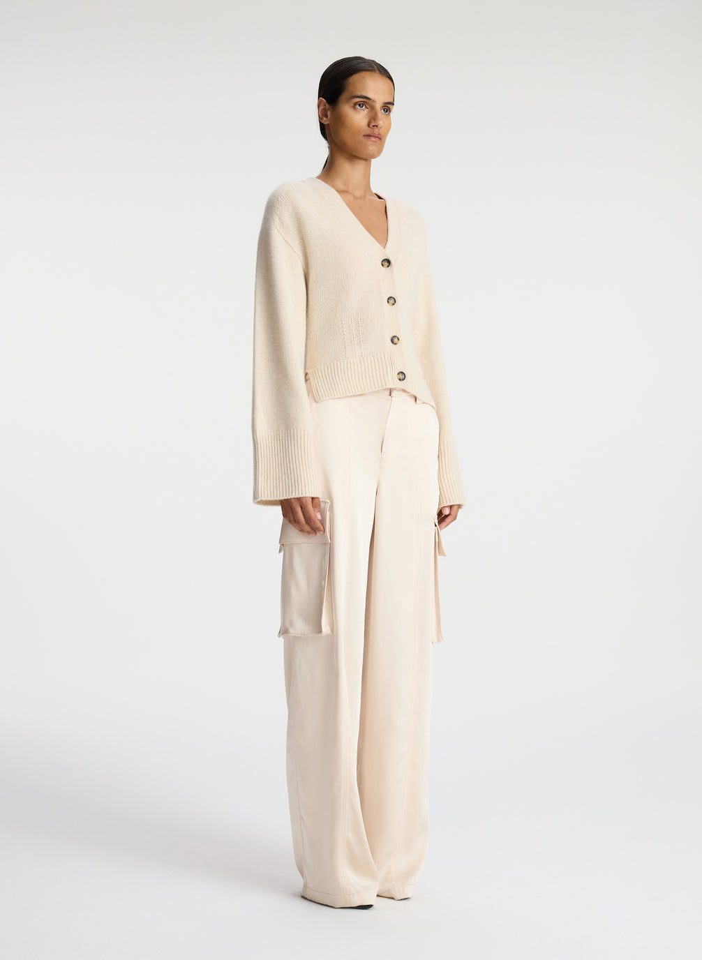 side view of woman wearing cream cardigan and off white satin cargo pants