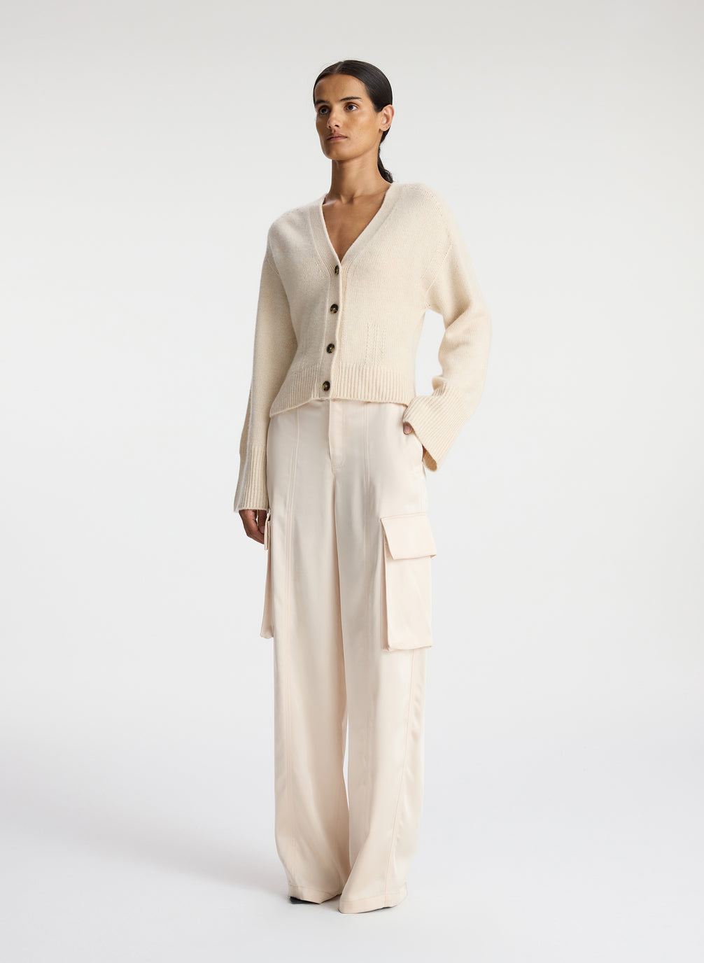 side view of woman wearing cream cardigan and off white satin cargo pants