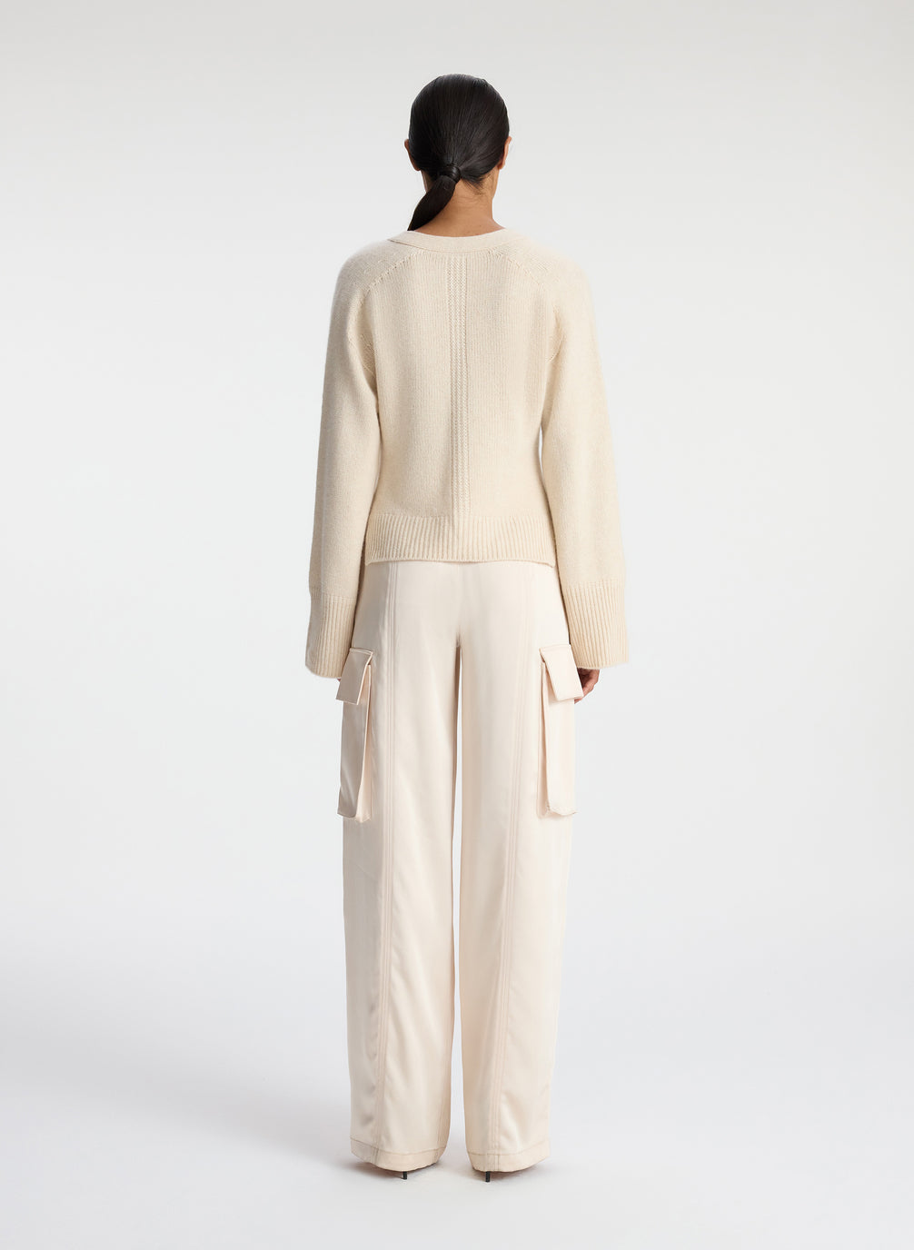 back view of woman wearing cream cardigan and off white satin cargo pants