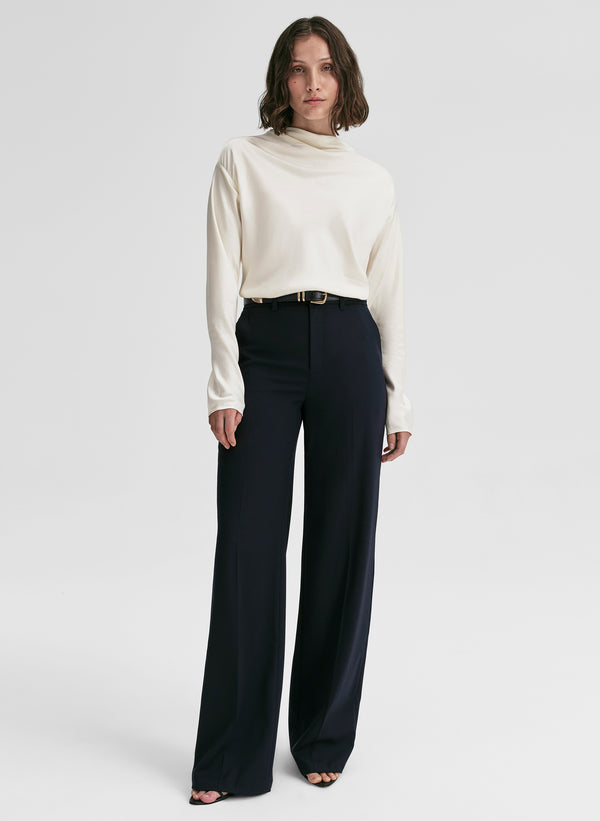 Woman wearing a white blouse and dark blue high-waisted pants on a white background