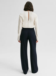 Woman wearing a white blouse and dark blue high-waisted pants on a white background
