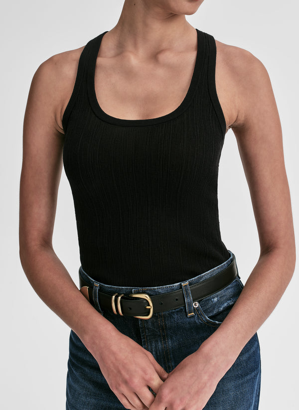 Person wearing a black tank top and blue jeans with a belt on a plain background