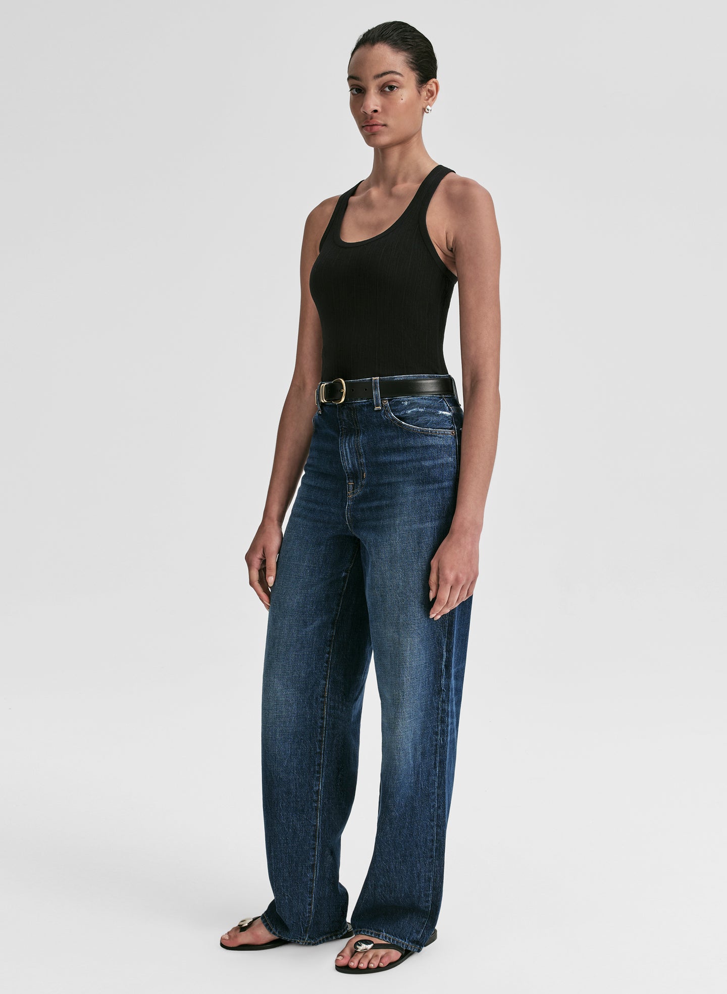 Woman wearing a black tank top and blue jeans on a white background