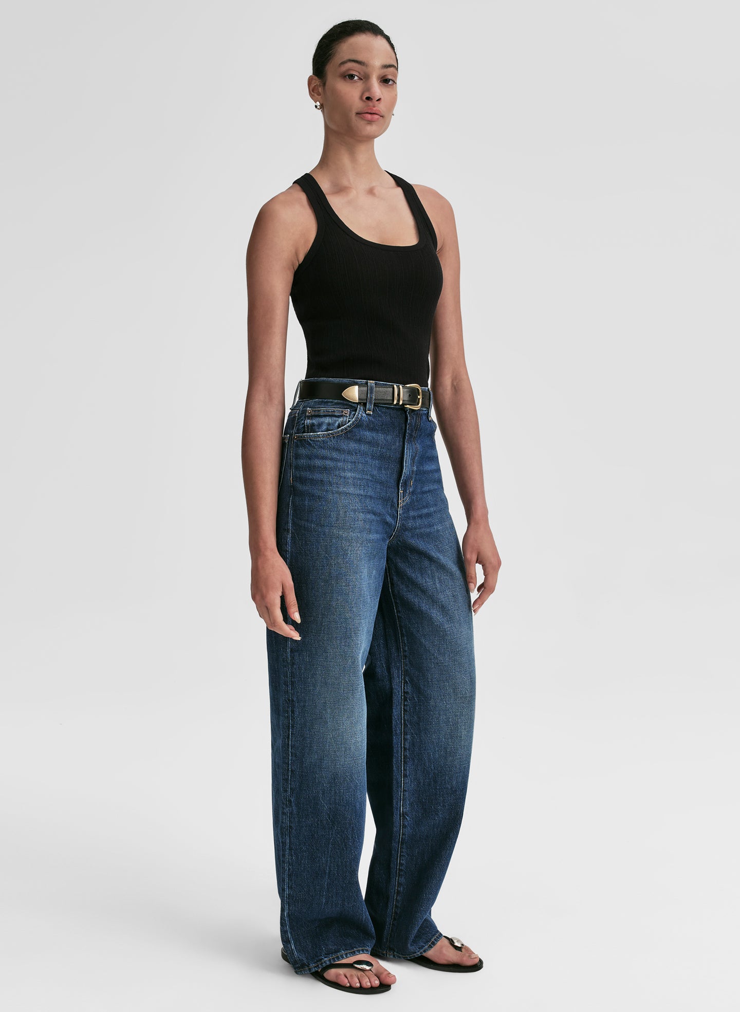 Woman wearing a black tank top and blue jeans on a white background