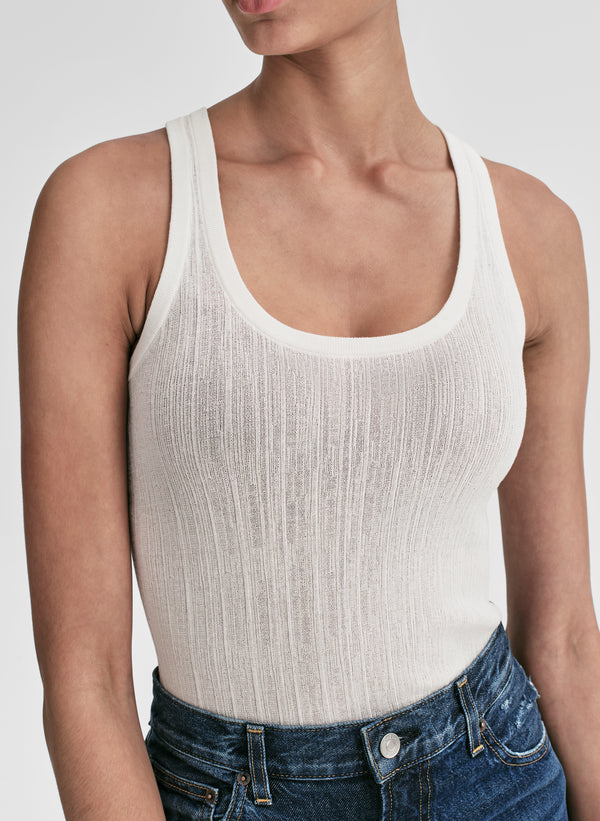 Woman wearing a white tank top and blue jeans on a plain background