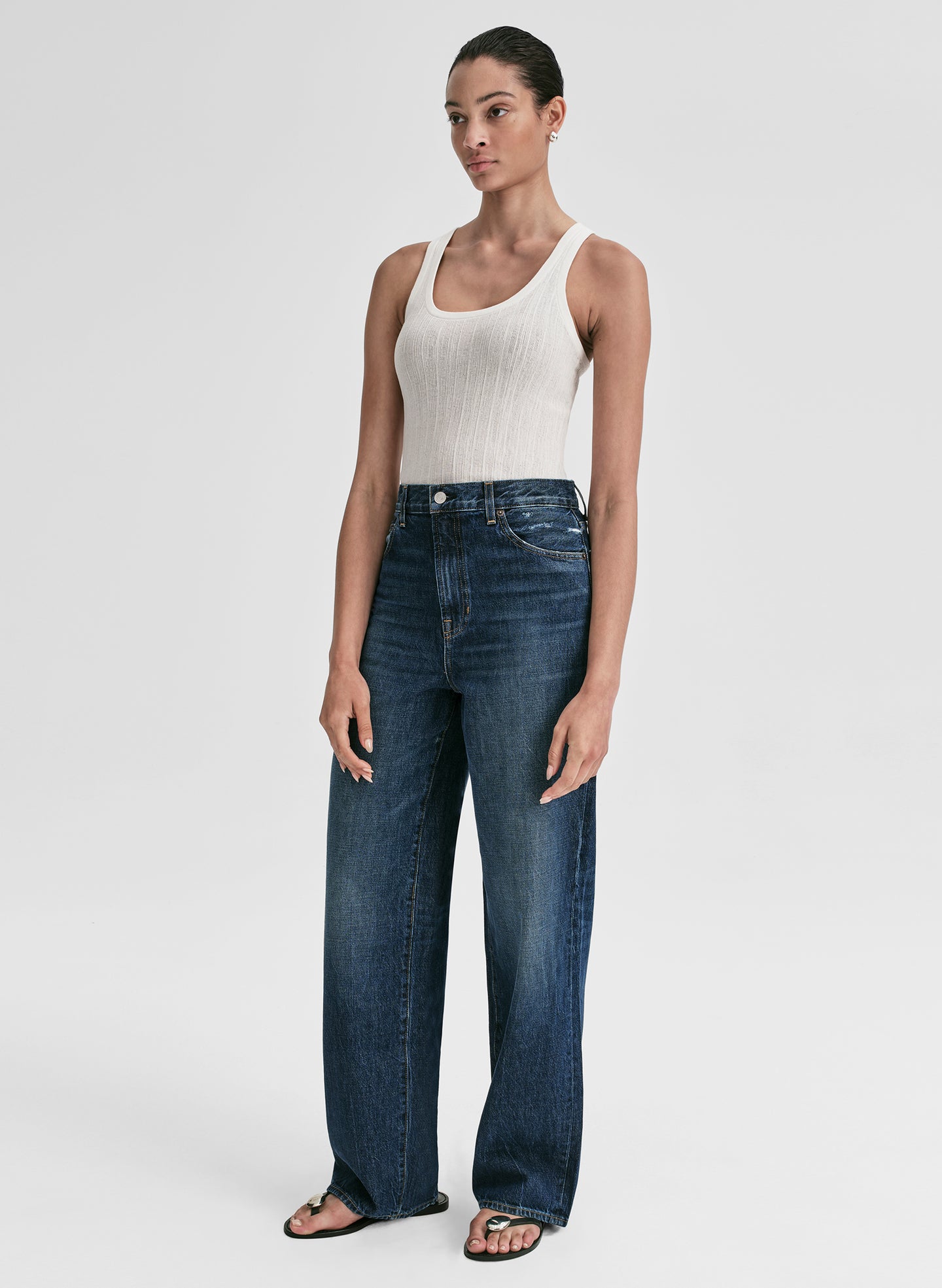 Woman wearing a white tank top and blue jeans on a plain background