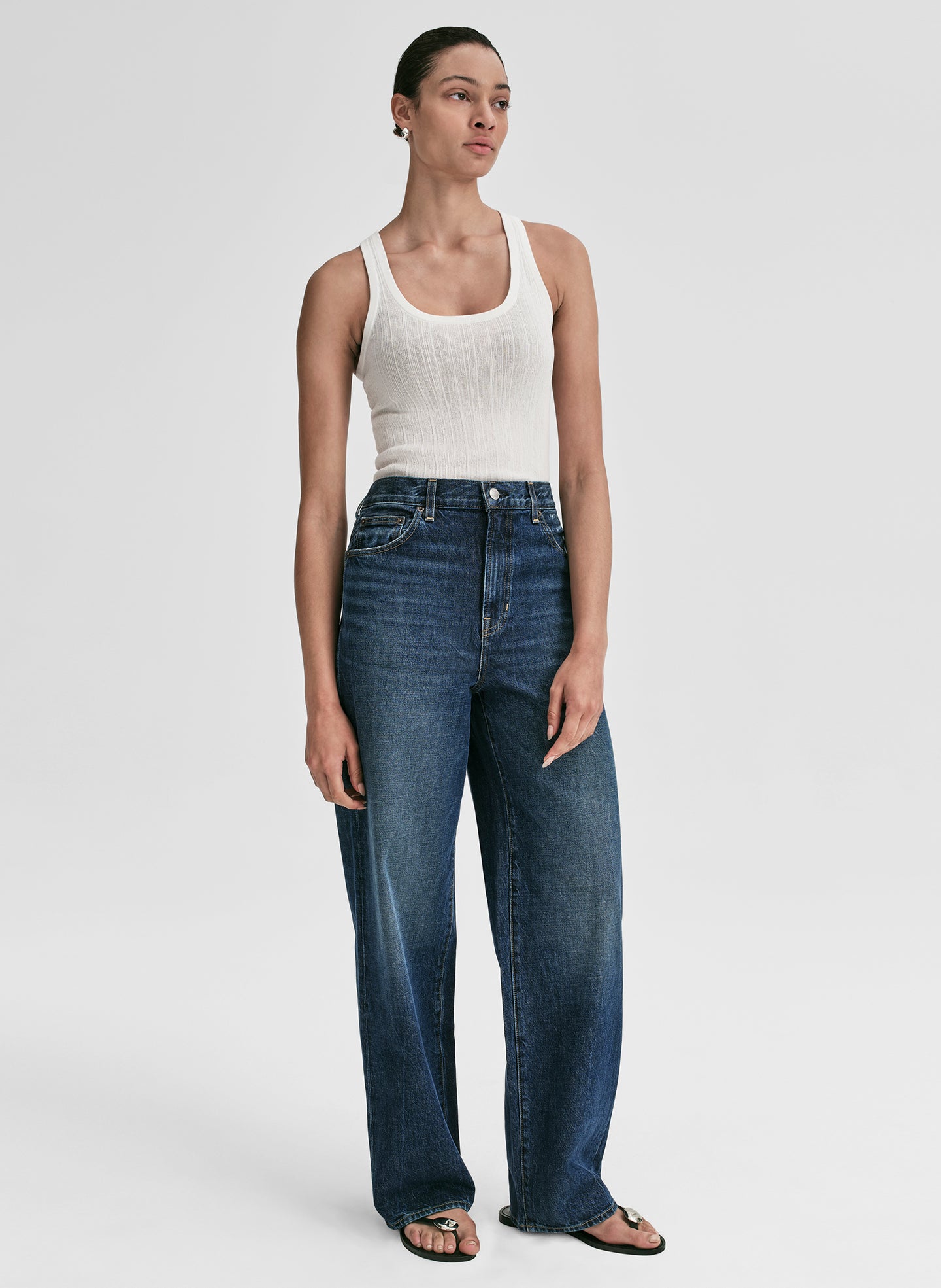 Woman wearing a white tank top and blue jeans on a plain background