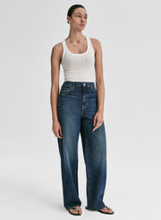 Woman wearing a white tank top and blue jeans on a plain background