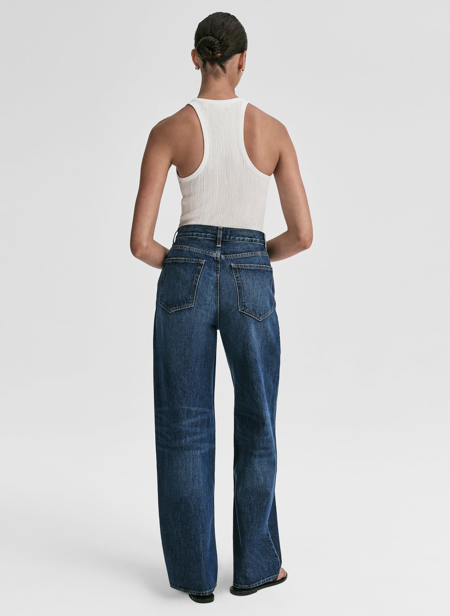 Woman wearing a white tank top and blue jeans on a plain background