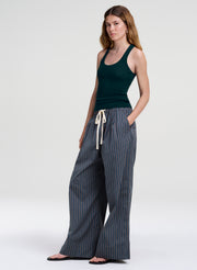 A woman modeling a dark green ribbed tank top and wide-leg pinstriped pants with a cream drawstring, standing against a light gray studio background.