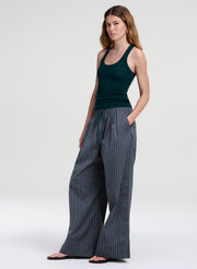 A woman modeling a dark green ribbed tank top and wide-leg pinstriped trousers in a studio setting with a light gray background.