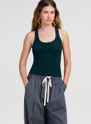 A woman modeling a dark green ribbed tank top and blue-and-white striped drawstring pants against a light gray studio background.