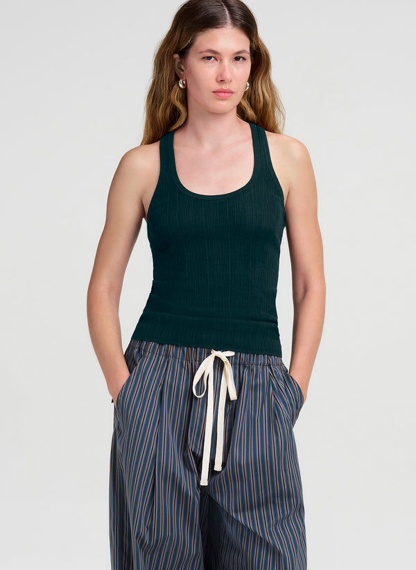 A woman modeling a dark green ribbed tank top and blue-and-white striped drawstring pants against a light gray studio background.