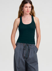 A woman modeling a dark green ribbed tank top paired with blue and gray vertically striped drawstring pants against a light gray studio background.