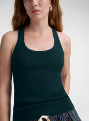 A close-up of a model wearing a dark forest green ribbed knit tank top against a light gray studio background.
