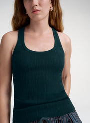 A close-up of a woman wearing a dark forest green ribbed knit tank top against a light gray studio background.