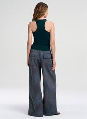 A woman shown from the back wearing a dark green ribbed tank top and slate blue wide-leg pinstripe pants with thin orange stripes, set against a plain light gray studio background.