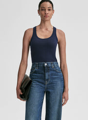 Woman wearing a navy tank top and blue jeans against a plain background