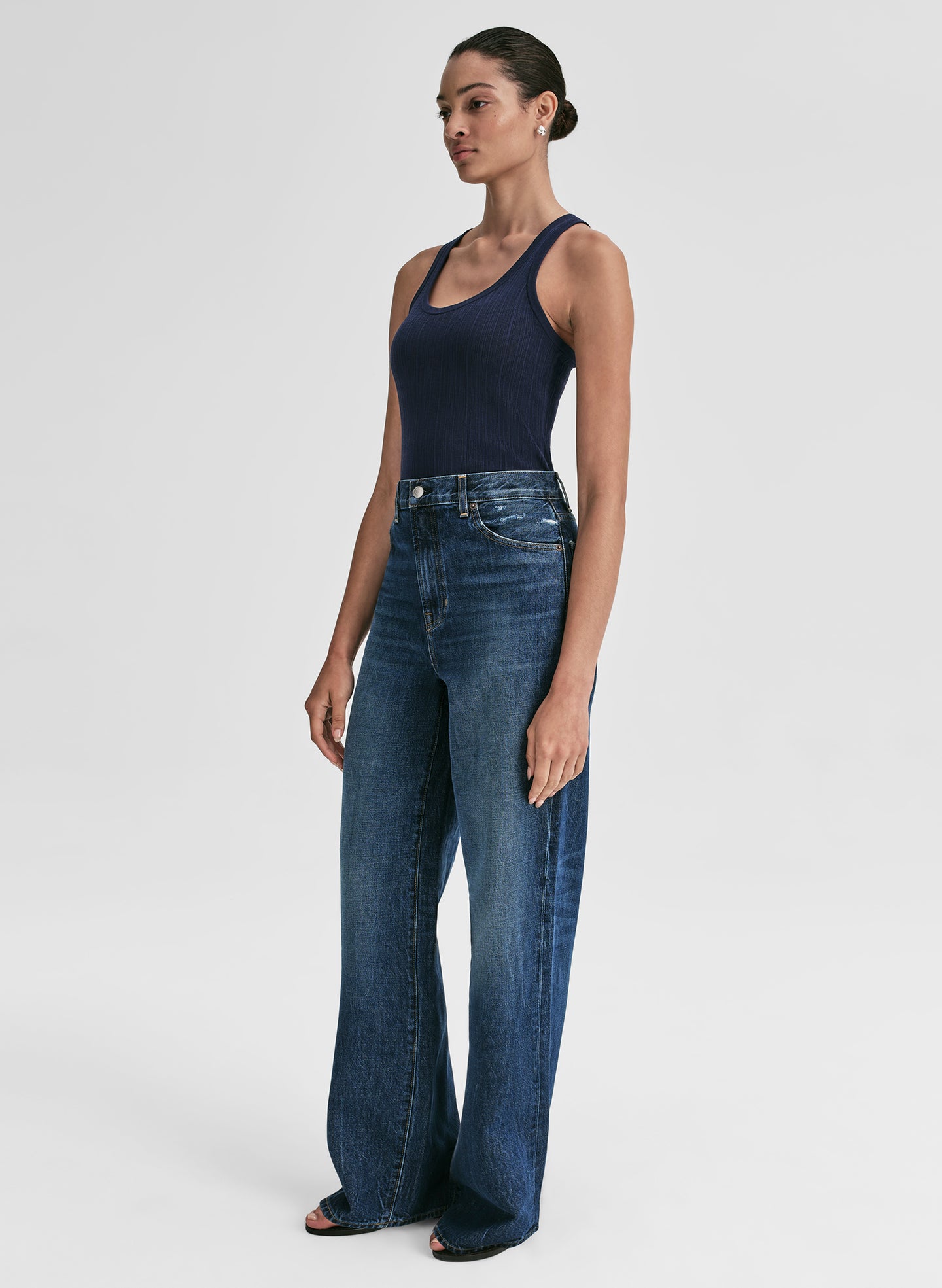 Woman wearing a navy tank top and blue jeans against a plain background