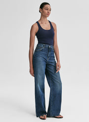 Woman wearing a navy tank top and blue jeans against a plain background