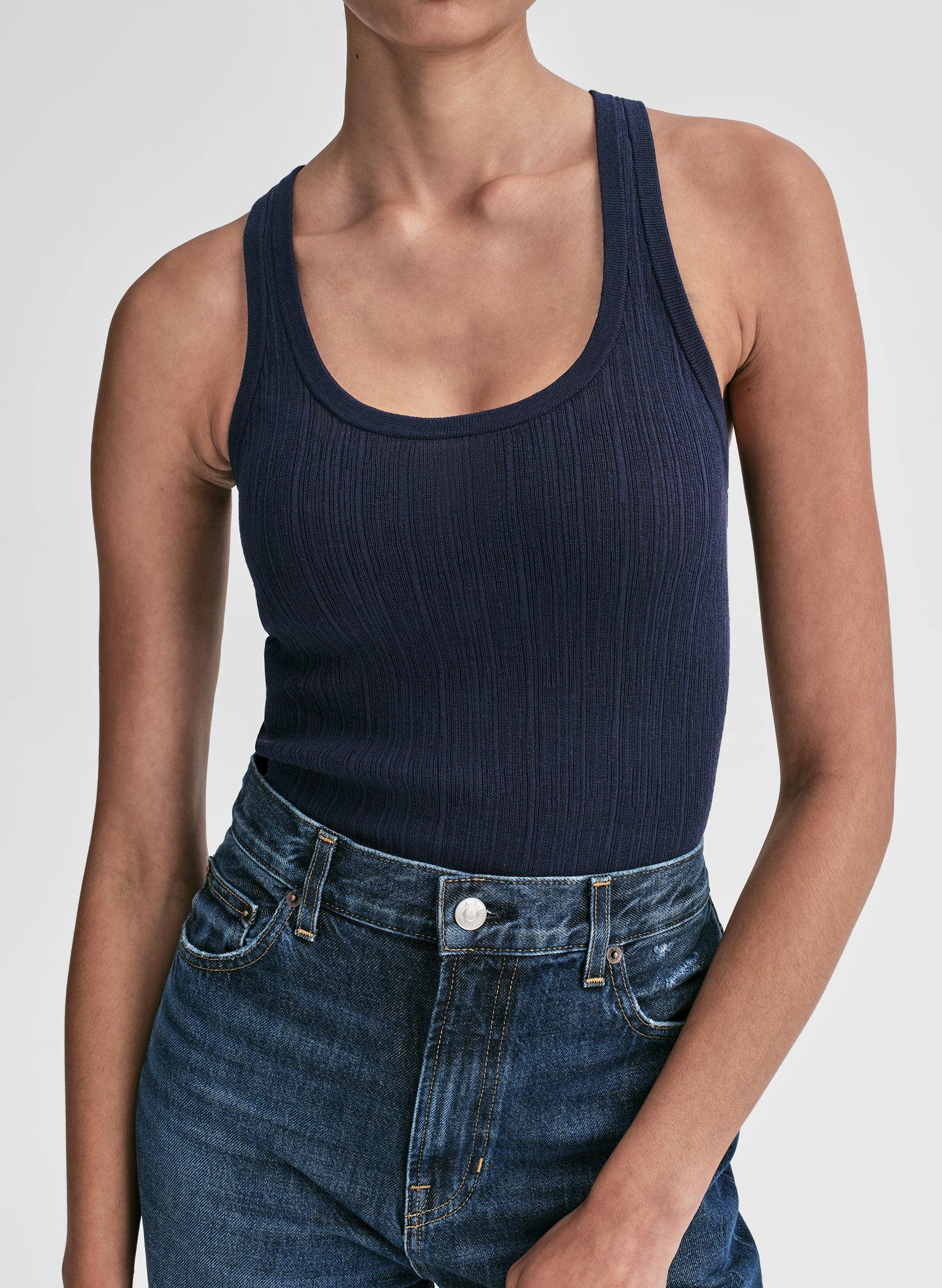Woman wearing a navy tank top and blue jeans against a plain background
