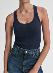 Woman wearing a navy tank top and blue jeans against a plain background
