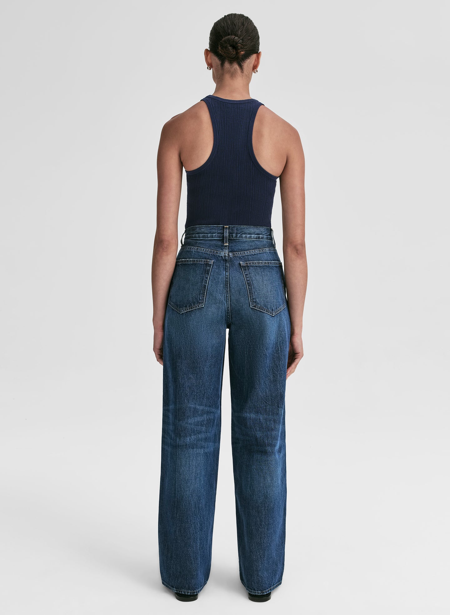 Woman wearing a navy tank top and blue jeans against a plain background