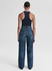 Woman wearing a navy tank top and blue jeans against a plain background