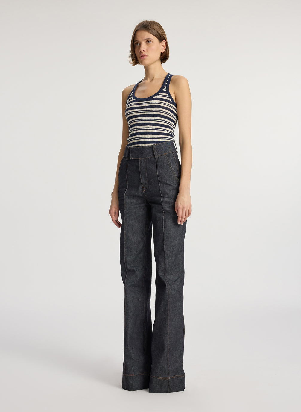 side view of woman wearing navy blue and white striped tank top with wide leg raw denim dark wash jeans