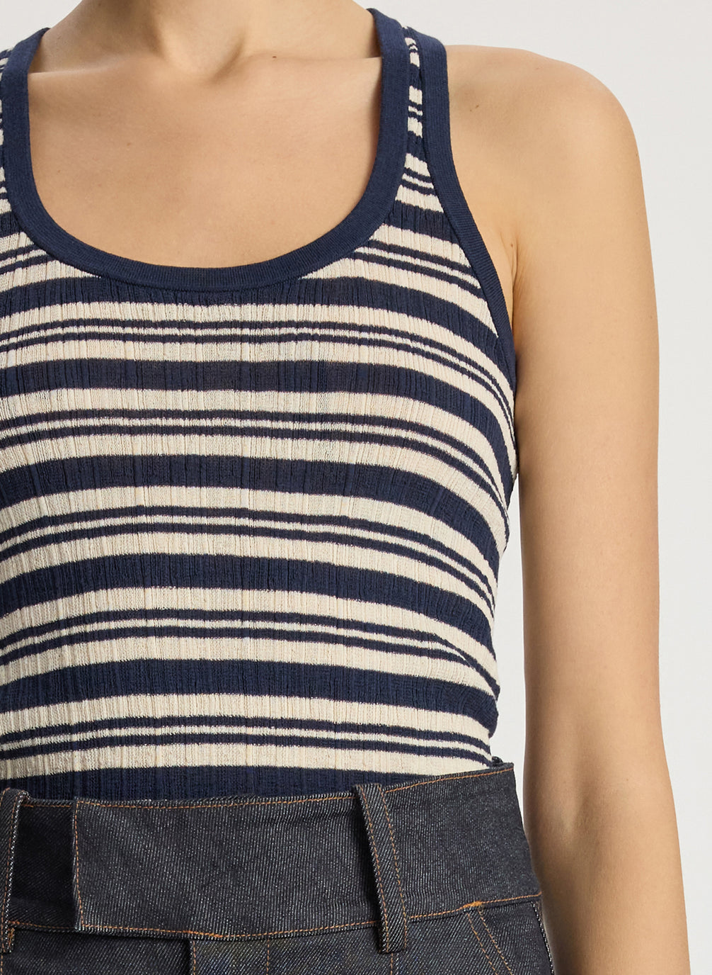 detail view of woman wearing navy blue striped tank top and dark wash raw denim jeans