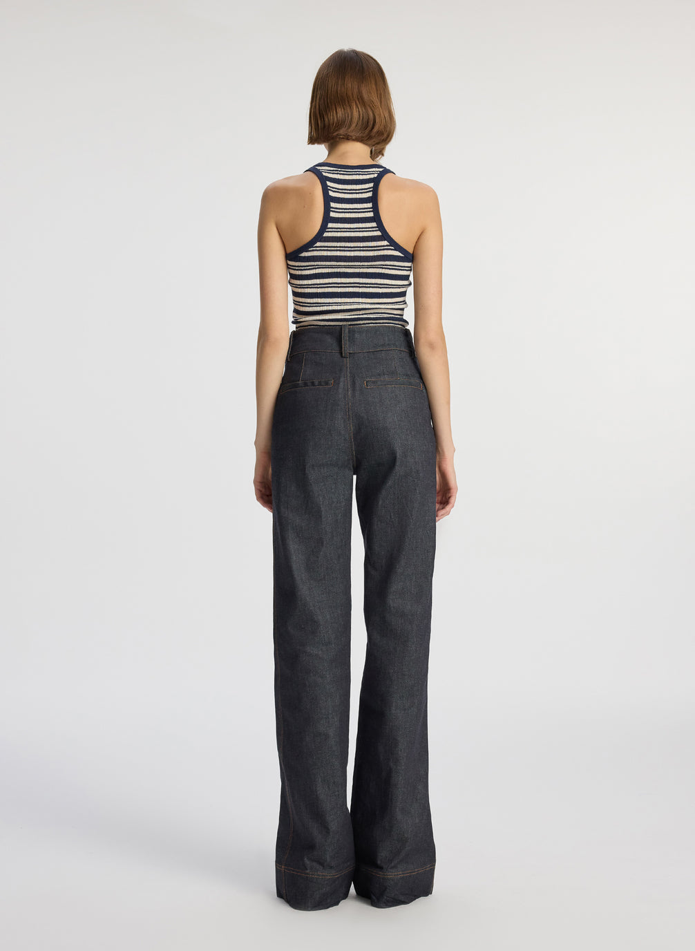 back view of woman wearing navy blue and white striped tank top with wide leg raw denim dark wash jeans