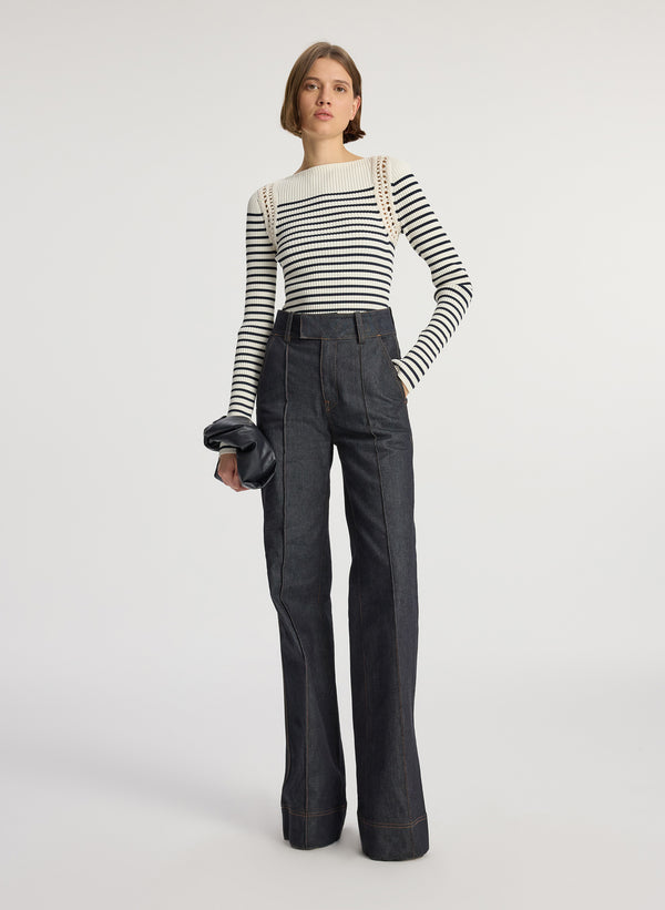 front view of woman wearing white and navy striped top with long bell sleeves and dark wash raw denim jeans