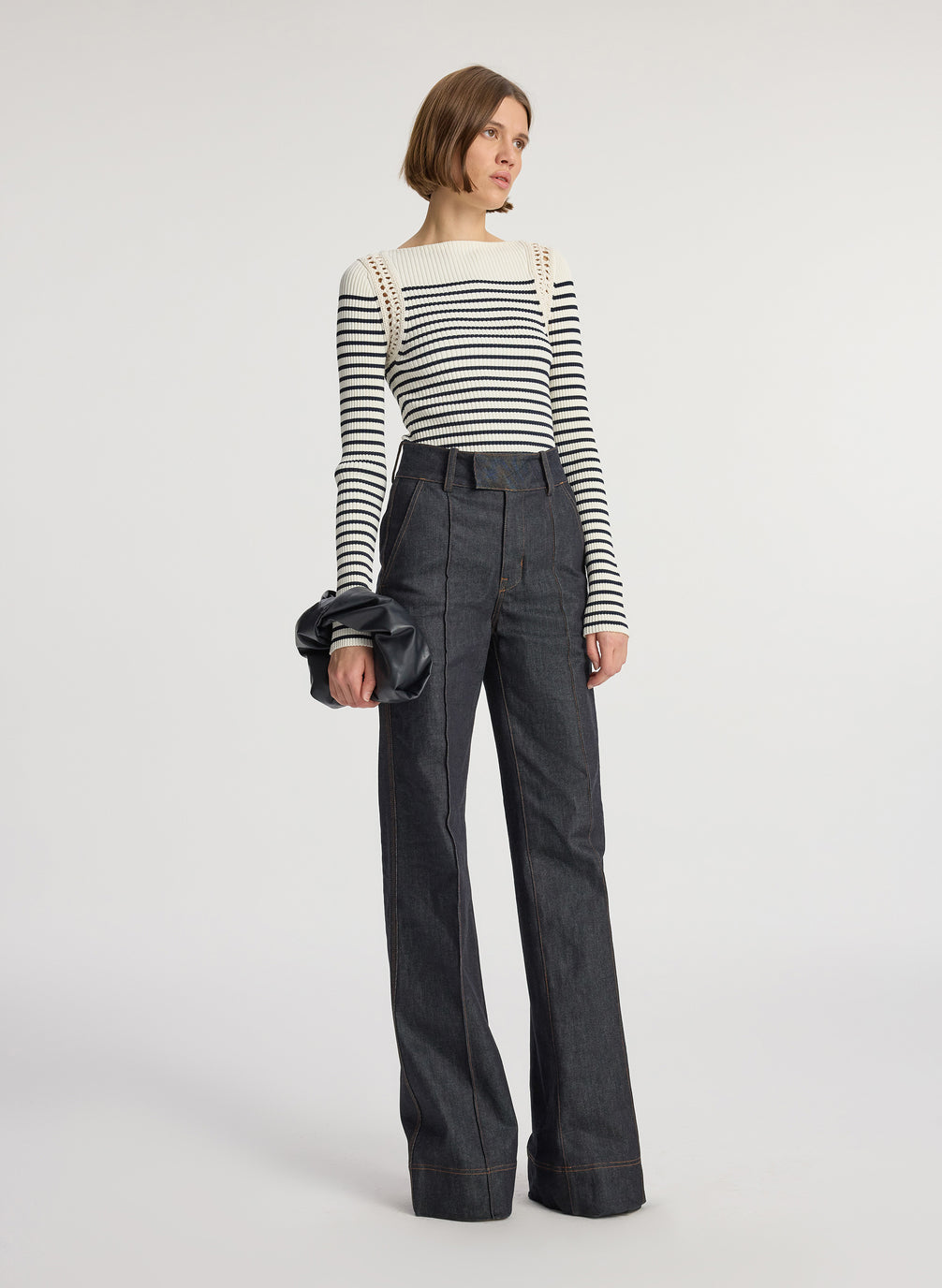 side view of woman wearing white and navy striped top with long bell sleeves and dark wash raw denim jeans