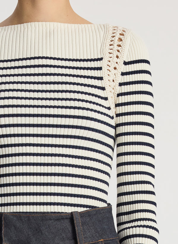 detail view of woman wearing white and navy striped top with long bell sleeves and dark wash raw denim jeans