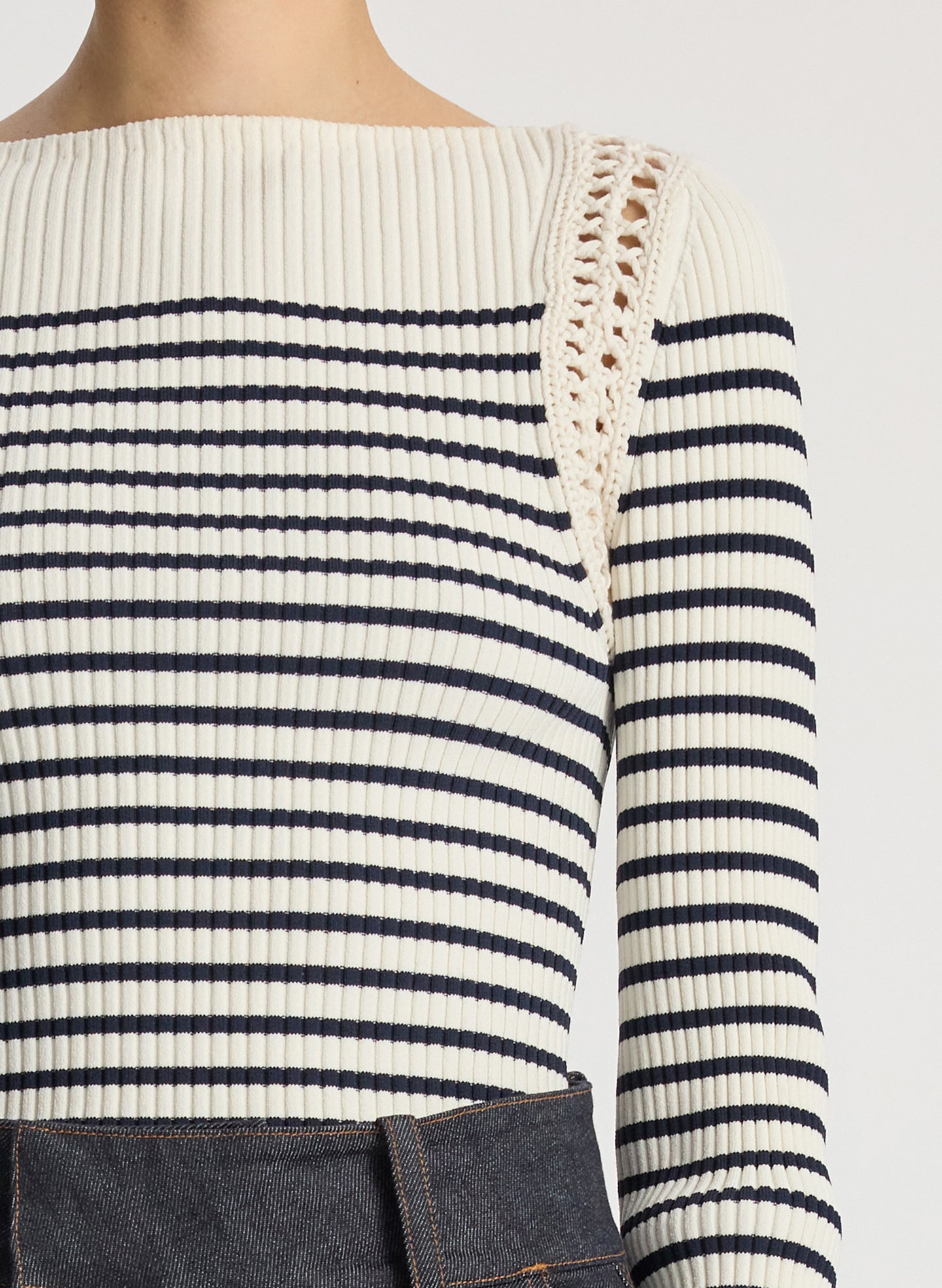 detail view of woman wearing white and navy striped top with long bell sleeves and dark wash raw denim jeans