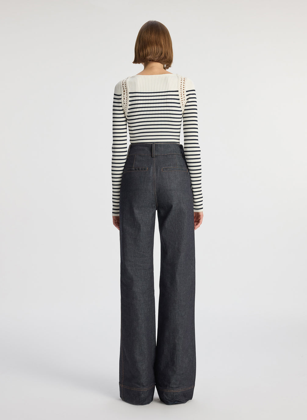 back view of woman wearing white and navy striped top with long bell sleeves and dark wash raw denim jeans