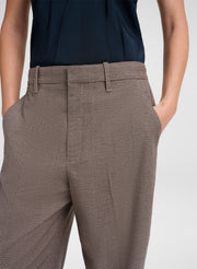 Close-up of a person wearing trousers with a fine brown and beige houndstooth pattern, paired with a dark navy top against a light gray studio background.