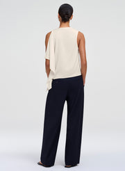 A model shown from the back wearing a white sleeveless draped top and dark navy wide-leg trousers, photographed against a seamless light gray studio background.