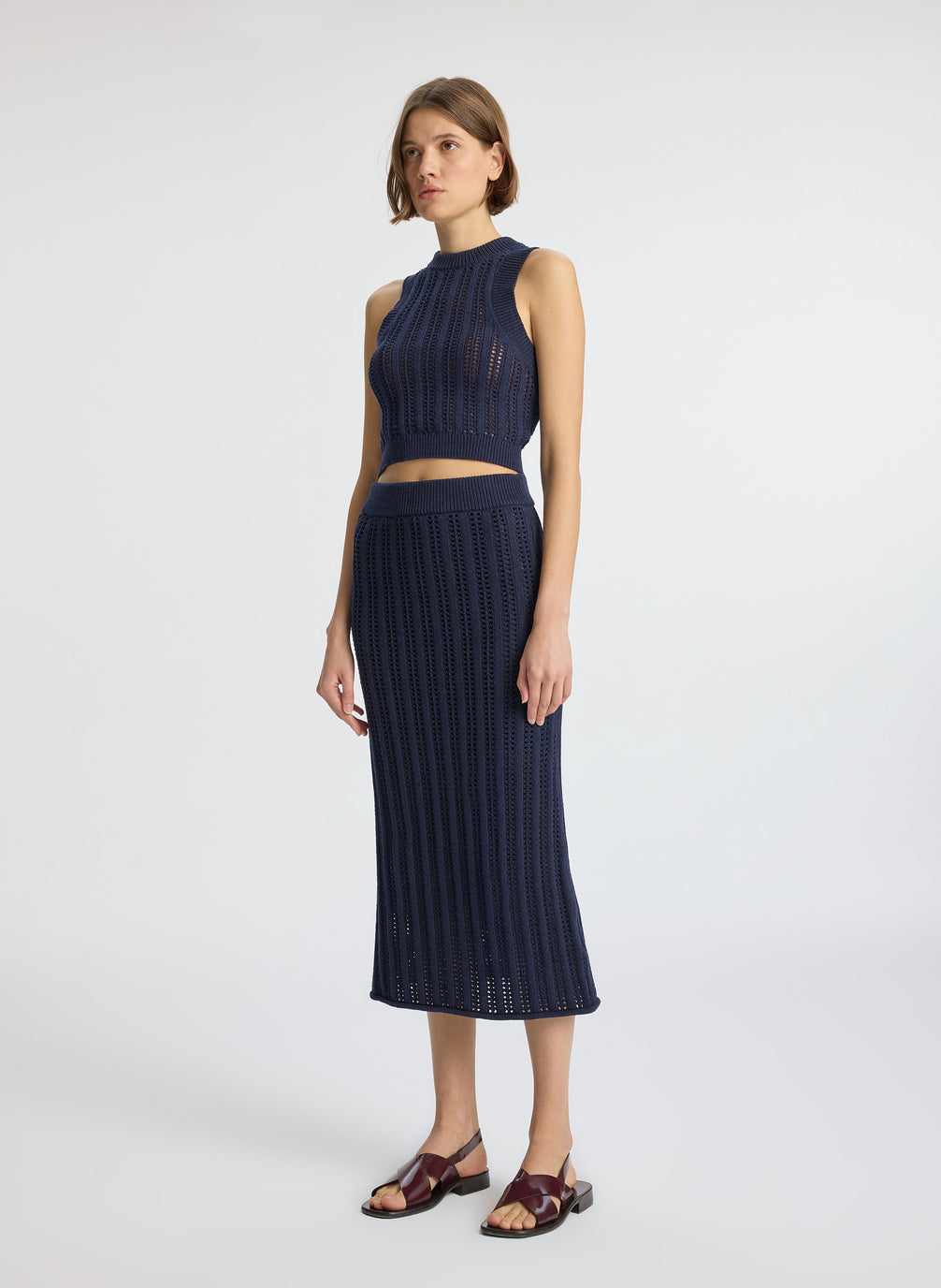 side view of woman wearing navy blue open weave tank top and matching skirt