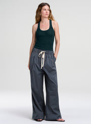 A woman modeling a dark green ribbed tank top and wide-leg striped pants with a cream drawstring, standing against a light gray studio background.